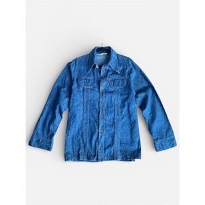 May include: A vintage blue denim shirt with long sleeves, a collared neckline, and two chest pockets. The shirt has a button-down front and is hanging on a black hanger. The denim has a classic, worn look.