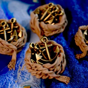 May include: Close-up of several decorative nautical-themed items. Each item features a gold-coloured anchor and other nautical elements nestled within a beige, rope-like material, set against a blue background.