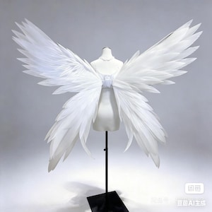 Puede incluir: Un par de grandes alas de plumas blancas exhibidas en un maniquí. Las alas están unidas a un corpiño blanco y están extendidas, mostrando su diseño en capas. Las plumas son suaves y esponjosas, creando un efecto dramático.