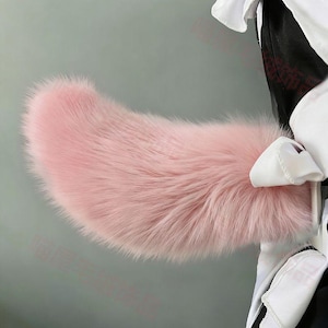 May include: A fluffy, pink faux fur tail, possibly for cosplay or costume. The tail is a soft, pastel pink and has a curved shape. It is attached to a black and white garment with white bows.