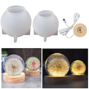 May include: Two clear silicone moulds for making resin sphere lamps. The moulds are round with a flat base and three small legs. A wooden base with a built-in LED light is also included. The image shows two finished resin spheres with dandelion designs inside.