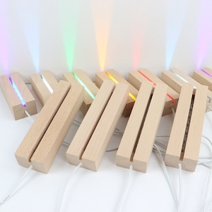 May include: A row of wooden light bases with LED lights in various colours, including purple, green, yellow, orange, red, pink, and blue. The bases are made of natural wood and have a simple, modern design.