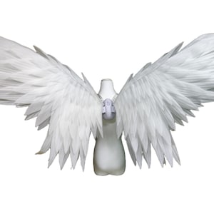May include: A pair of large, white, feathered wings attached to a central harness. The wings feature layered, pointed white feathers that extend outward in a wide span. The harness is a light gray, molded structure positioned at the center.