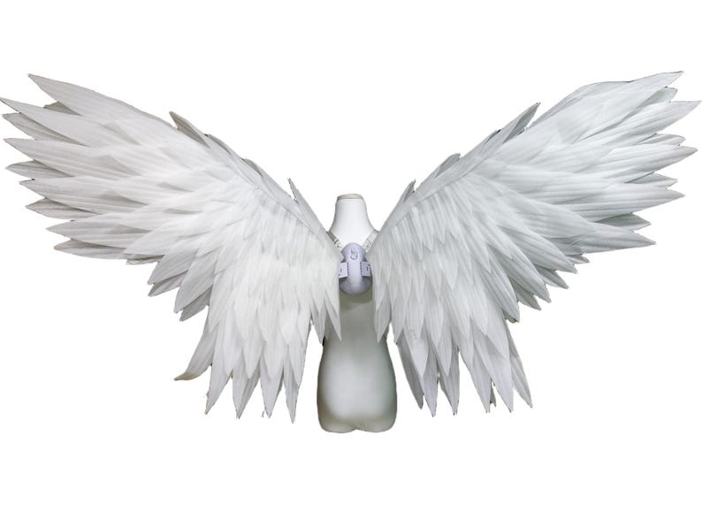 May include: A pair of large, white, feathered wings attached to a central harness. The wings feature layered, pointed white feathers that extend outward in a wide span. The harness is a light gray, molded structure positioned at the center.