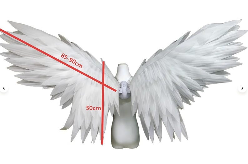 May include: Large white feathered wings attached to a central harness. The wingspan is marked with red lines indicating a width of 85-90 cm and a vertical height of 50 cm. The structure is mounted on a white torso mannequin form for display.