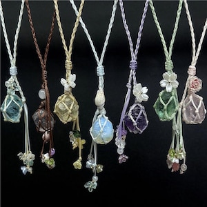 May include: A collection of handmade gemstone necklaces. Each necklace features a unique, colorful crystal encased in a macrame net, suspended from a cord. Embellishments include small beads and floral accents. The gemstones vary in color, including blue, brown, yellow, purple, green, and pink.