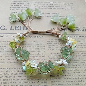 May include: A green and white beaded bracelet with a brown cord and small green and white flowers. The bracelet is on a piece of paper with text that reads "G. LEHMEN, INDIA" and "NGLE TO OR QUESTION."