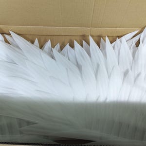 May include: A collection of white, pointed, feather-like foam pieces arranged in a layered, overlapping pattern. The individual elements are elongated, tapered, and have a smooth, matte texture, creating a dense, wing-like structure.