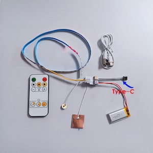 Puede incluir: Un conjunto de componentes electrónicos, que incluye una tira LED azul, un mando a distancia, un conector Tipo-C y una pequeña batería. El mando a distancia tiene botones para encendido, brillo y temporizador. El texto "Type-C" es visible.
