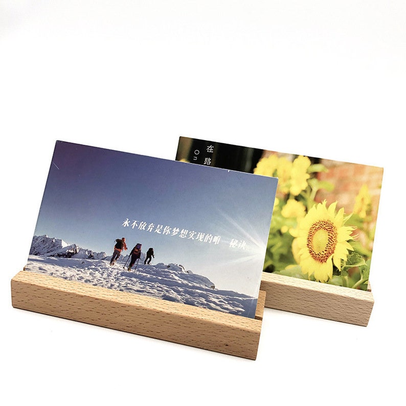 Peut inclure: Deux supports photo en bois sur fond blanc. Le support de gauche pr&eacute;sente une photo de trois personnes faisant de la randonn&eacute;e dans un paysage montagneux enneig&eacute;. La photo contient du texte chinois qui se lit comme suit : "Tous les voyages ne vous m&egrave;nent pas &agrave; l'endroit o&ugrave; vous voulez aller, mais ils vous m&egrave;nent tous quelque part." Le support de droite pr&eacute;sente une photo d'un tournesol jaune dans un champ.