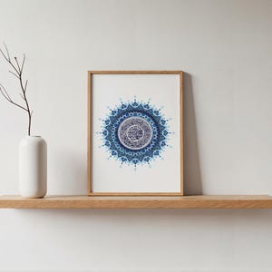 Affiche islamique minimaliste représentant la Sourate Al Fatiha en mandala bleu, encadrée en bois clair et posée sur une étagère moderne. Cette décoration murale coranique s’intègre parfaitement dans un intérieur épuré, scandinave ou contemporain. Elle répond au besoin d’un art islamique discret mais puissant, apportant sérénité et élégance à votre maison. Fichier numérique haute qualité 300 DPI prêt pour impression professionnelle.