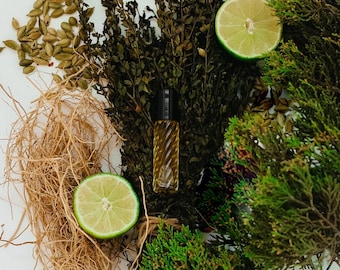 Pode incluir: Um frasco de vidro de óleo essencial com um topo de bola rolante preto, rodeado por folhas verdes, galhos marrons e fatias de limão. O frasco está sobre uma superfície branca.