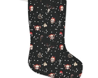 Puede incluir: Calcetín navideño negro con un patrón repetido de calaveras con gorros de Papá Noel, calaveras de reno, esqueletos, coronas y bastones de caramelo. Puntos blancos dispersos por la superficie. Un lazo blanco está unido en la parte superior.