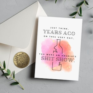 May include: A humorous birthday card with a watercolor background featuring a broken wine bottle. The card reads "Just think, years ago on this very day, you were an absolute shit show."
