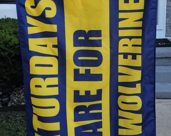 May include: A blue and yellow flag with the text "Saturdays Are For The Wolverines".