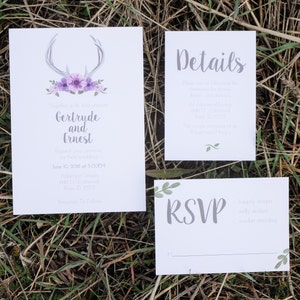 May include: Wedding invitation suite with a white background. The main invitation features gray antlers, purple flowers, and the names "Gertrude and Ernest." Additional cards include "Details" and "RSVP" with leaf accents. The text is in gray.