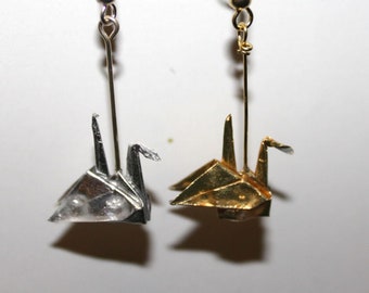 May include: A pair of silver and gold origami crane earrings. The earrings are hanging from silver hooks.