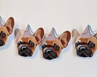 May include: A string of French bulldog head cutouts with party hats. The dog heads are brown, black, and white, strung on a natural twine. The party hats are pink with white polka dots and blue trim.