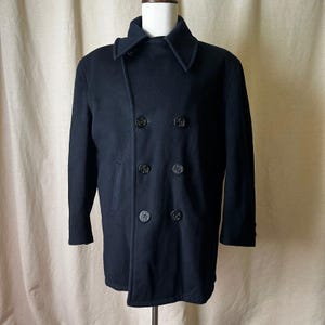 May include: A navy blue double-breasted wool coat with six dark buttons. The coat has a notched collar and two side pockets. The coat is displayed on a mannequin. A classic outerwear garment.