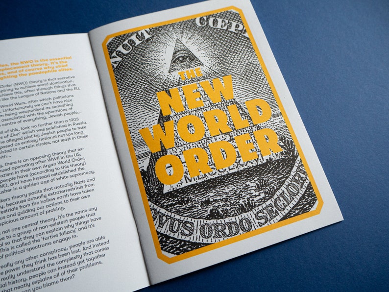 May include: A black and white illustration of a pyramid with an eye at the top. The pyramid is surrounded by a yellow border with the text "The New World Order" in large yellow letters. The text "Novus Ordo Seclorum" is printed in black at the bottom of the image.
