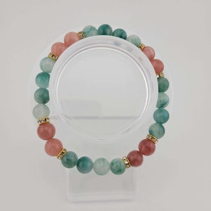 May include: A bracelet made of green and pink gemstone beads with gold accents and clear rhinestones.