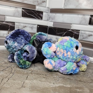 May include: Two plush octopus toys, one blue and green and the other pink, purple, and green. The octopus toys are made of soft, fuzzy fabric and have large, round eyes.