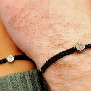 May include: Two black cord bracelets with silver charms. The charms have the letters "P" and "C" on them.