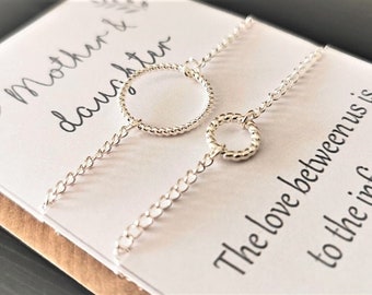 May include: Two silver bracelets with a circle charm on each. The bracelets are on a white card with the text "Mother & daughter The love between us is to the infinity SJ Supreme Joy Gifts".