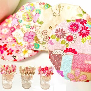 Op de afbeelding: Set van vijf stoffen hoezen voor glazen of potten. De hoezen zijn gemaakt van roze, witte en blauwe stof met bloemenpatronen. De hoezen hebben allemaal verschillende patronen.