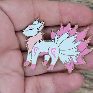 May include: A white and pink enamel pin of a nine-tailed fox with a pink and white fluffy tail. The fox has pink accents on its face and body.