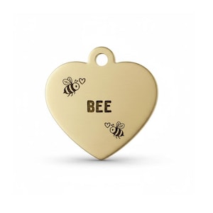 May include: A heart-shaped, gold-coloured pet tag with the word "BEE" in the centre. Two small bee illustrations are on either side of the word. The tag has a small hole at the top for attachment.