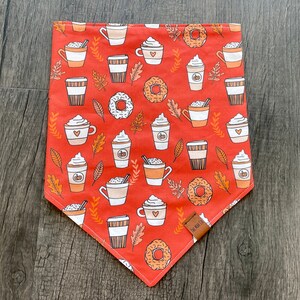 May include: Orange bandana with a pattern of coffee cups, donuts, and fall leaves. The bandana has a brown tag with the text "The Well Fed Pup" on it.