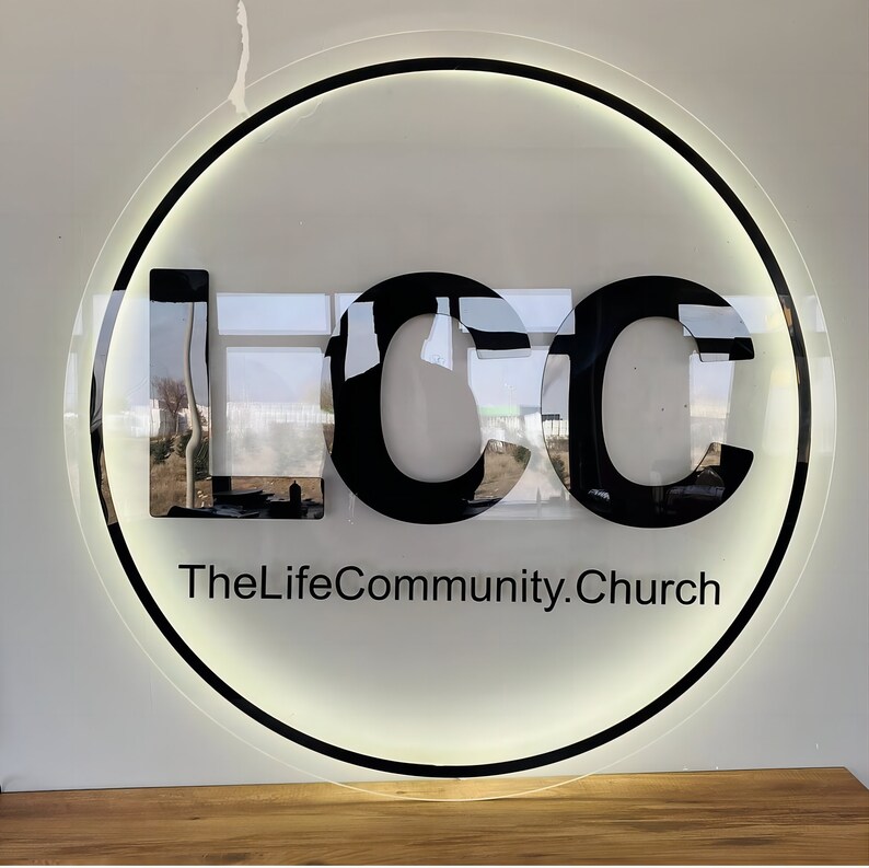 May include: A black and white circular sign with the letters "LCC" in a bold font. The text "TheLifeCommunity.Church" is written below the letters.