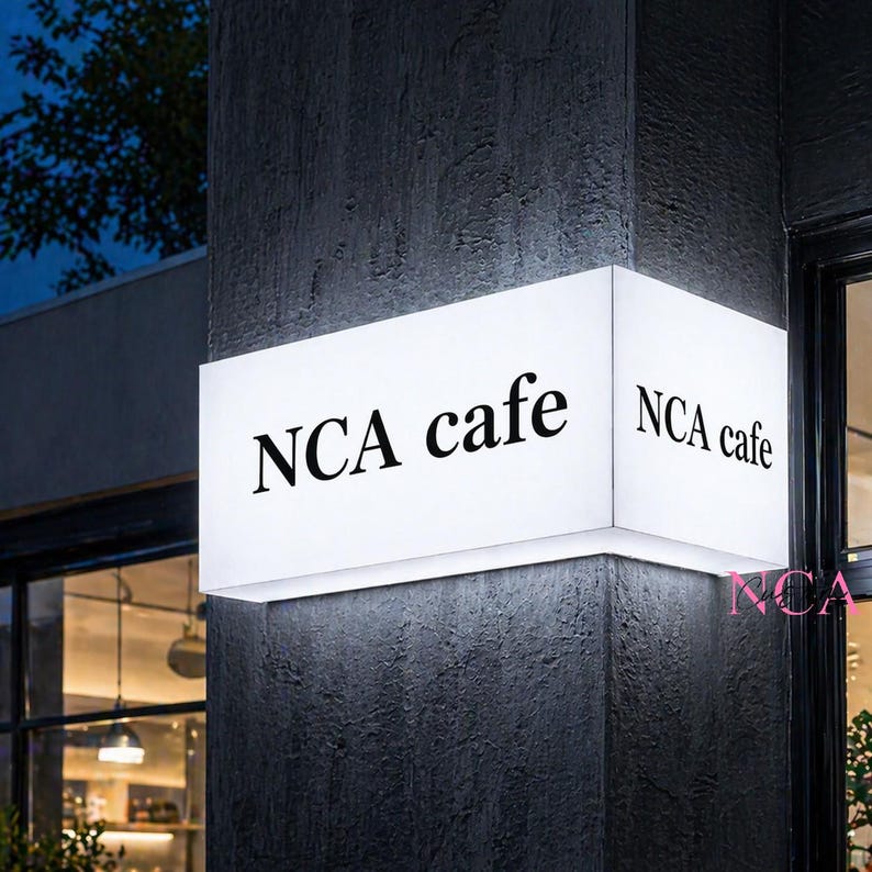 Puede incluir: Letrero rectangular blanco iluminado con el texto "NCA cafe" en letras negras. El letrero est&aacute; montado en una pared texturizada de color gris oscuro, con el nombre del caf&eacute; visible desde m&uacute;ltiples &aacute;ngulos.