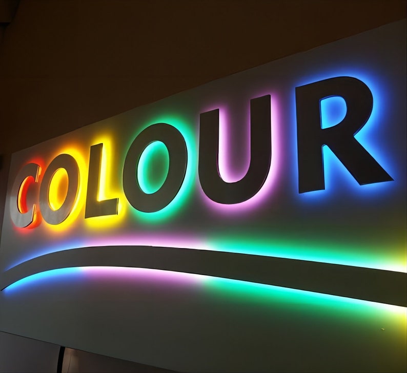 K&ouml;nnte beinhalten: Ein wei&szlig;es Schild mit dem Wort "COLOUR" in gro&szlig;en, erhabenen Buchstaben. Jeder Buchstabe ist in einer anderen Farbe des Regenbogens umrandet, beginnend mit Rot und endend mit Blau.