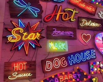 May include: A wall decorated with neon signs featuring various phrases and designs, including "Hot", "Star", "Happiness", "Dog House", "Cabaret", and "You".