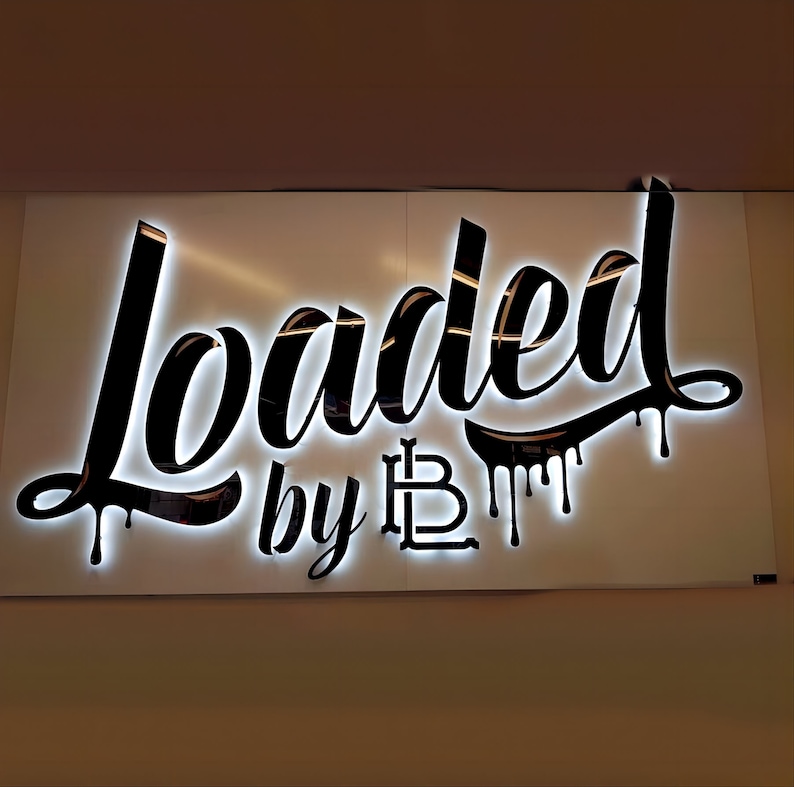K&ouml;nnte beinhalten: Ein wei&szlig;es Schild mit schwarzer Beschriftung, auf dem in einer stilisierten Schrift "Loaded by LB" steht. Die Buchstaben sind wei&szlig; umrandet und haben einen tropfenden Effekt.