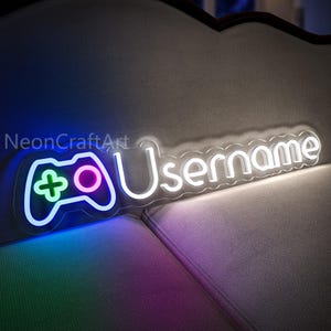 May include: White neon sign with a gamer controller and the word "Username" in a white neon font. The sign is lit up and has a blue, green, and pink glow.