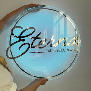 May include: A round, clear, backlit sign with a gold border and the word "Eterna" in a stylized black font. The text "Radio Frequency" is written in smaller black font below the word "Eterna".