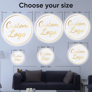 May include: A white wall with a selection of round, white, illuminated signs with a gold outline and the text "Custom Logo" in gold lettering. The signs are available in different sizes, ranging from 16 inches to 80 inches in diameter.