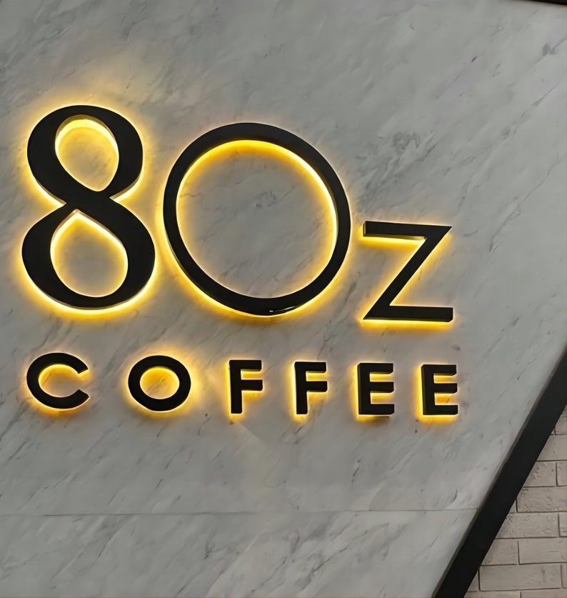 K&ouml;nnte beinhalten: Ein schwarzes und gelbes Schild mit dem Text "8OZ COFFEE" auf einem wei&szlig;en Marmorhintergrund.
