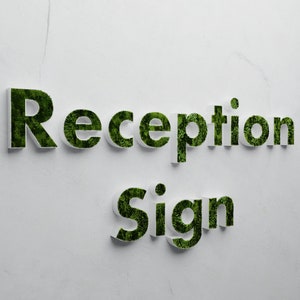 May include: White sign with the words "Reception Sign" in green letters made of moss.