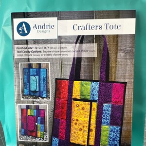 May include: A colorful tote bag with a tool caddy pocket. The tote bag is made of patchwork fabric in shades of red, pink, purple, yellow, green, and blue. The tote bag is 14 inches wide and 16 inches high. The tool caddy pocket is square shaped and has a snap closure. The tote bag is made with a pattern that can be used to create similar bags.