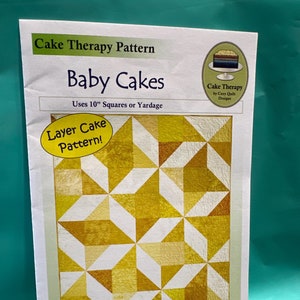 May include: A quilting pattern for a "Baby Cakes" quilt, using a layer cake pattern. The quilt is made with 10-inch squares and features a geometric design with yellow and white squares. The pattern is designed by Georgette Dell'Orco and includes sizes for baby, throw, twin, and queen quilts.