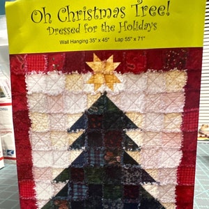 May include: A Christmas-themed wall hanging with a patchwork design. The image features a Christmas tree made of dark green fabric, topped with a gold star. The text "Oh Christmas Tree! Dressed for the Holidays" is displayed at the top.