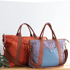 May include: Two tote bags with brown handles and straps. The larger bag is orange with a quilted pattern, and the smaller bag is blue with a geometric design. The text "OXBOW TOTE" is at the top.