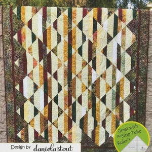 May include: A geometric quilt with a diamond pattern. The quilt features vertical stripes in shades of cream, gold, burgundy, and green. The border is a dark green with a floral pattern. The text "Design by daniela stout" is visible.