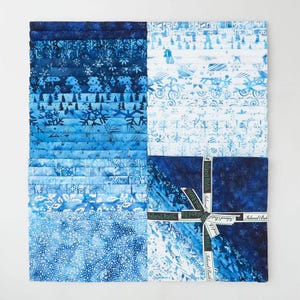 May include: A collection of blue and white batik fabric squares. The fabric features various winter-themed patterns, including snowflakes and trees. The fabric is tied with a ribbon that says "Island Batik".