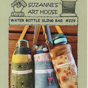 May include: Three water bottle sling bags with different patterns and colors hang against a wooden background. The bags have zippered pockets and adjustable straps. The text "SUZANNE'S ART HOUSE WATER BOTTLE SLING BAG #229" is at the top.