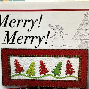 May include: A red and green quilted table runner with a white center panel featuring a row of five embroidered Christmas trees. The text "Merry! Merry!" is printed above the runner.
